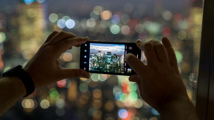 Unidentified man taking a photo of Tokyo skyline with his smart phone from Tokyo Tower, Japan