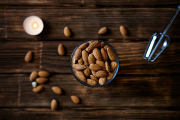 Dried almond nuts in a glass on a plank rustic background. Nearby there is a whisk and a candle. Country style