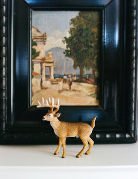 Deer toy miniauture in front of painting on shelf at home