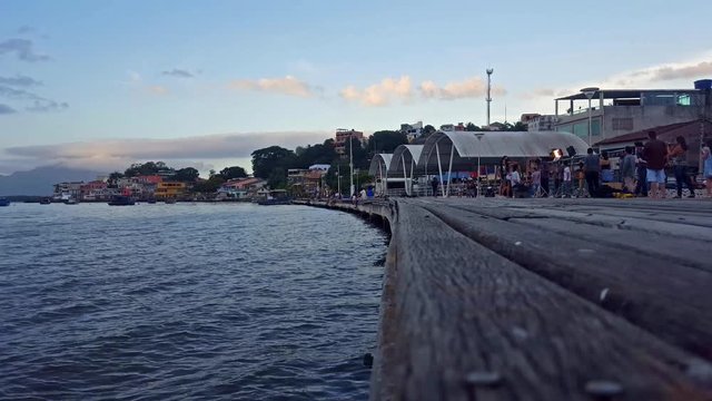 Scene of the Caieiras Island, Vit&oacute;ria-ES, view of the deck in a late afternoon. People interacts with each other in the background. Several houses and boats. Clear sky with a few c