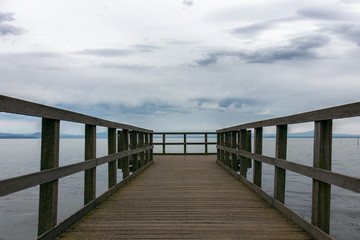Fototapeta na wymiar Beautiful view of Lake Trasimeno from the pier. The sky is clouded over and calm water, no people. Nostalgic mood. Umbria, Italy