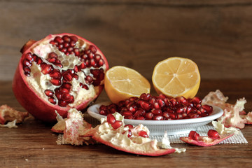 Ripe pomegranate and lemon on a ceramic plate. Close-up, wooden table and rustic background.