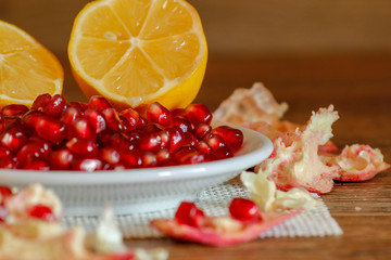Ripe pomegranate and lemon on a ceramic plate. Close-up, wooden table and rustic background.