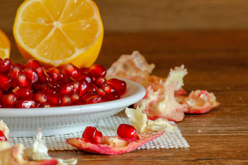 Ripe pomegranate and lemon on a ceramic plate. Close-up, wooden table and rustic background.