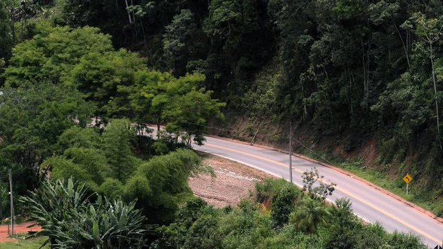 Scene of a road with trees around. Vehicles go both ways.