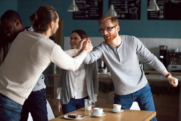 Fototapeta na wymiar Excited millennial friends greeting, hanging together in cafe, smiling guy get acquainted with colleague at friendly meeting in coffeeshop, diverse students reunited in cafeteria embracing say hello