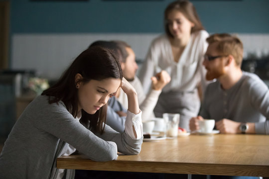 Upset young girl sit alone at coffee table in cafe feeling lonely or offended, sad female loner avoid talking to people, student outsider suffer from discrimination, lacking friends or company