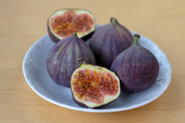 Common fig Ficus carica ripened violet fruits, group of figs on small white plate on wooden table