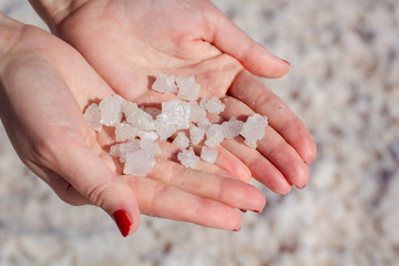 Female hand holding natural salt crystals on the background of a salt lake view from above