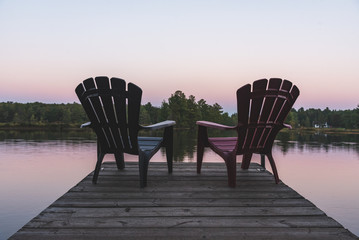 Two Adirondack chairs sitting on a dock - Muskoka, Ontario, Canada.