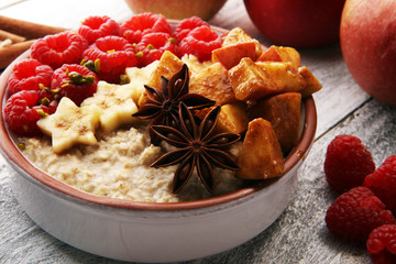Bowl of oatmeal porridge with banana, apples,raspberries coconut and caramel sauce on rustic table, hot and healthy food for Breakfast