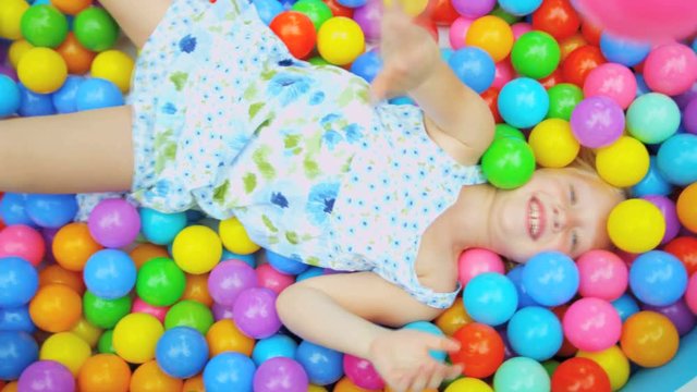 Portrait of cute blonde Caucasian child covered in multi coloured plastic balls in big paddling pool 