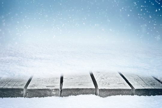 Wooden table in snowdrift and folling snowflakes from the sky