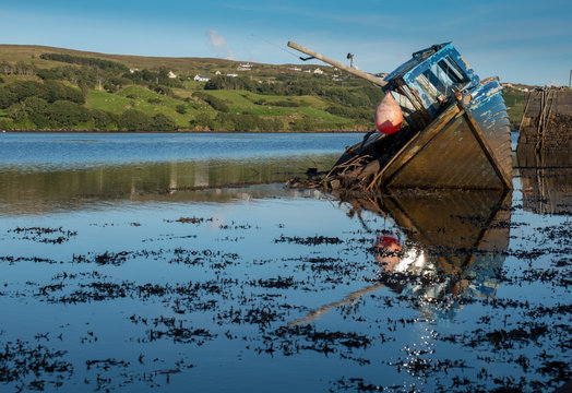 Wreck of a fishing boat on the wild atlantic coast of Ireland.  Faded paint blue ship in lying sideways with perfect reflection in low tide waters.