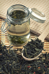 Jar with brewed green tea and wooden spoon with dry tea leaves