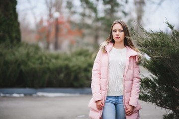 Beautiful young girl in white sweater and pink jacket walking in the Park.