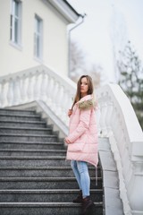 Beautiful young girl in white sweater and pink jacket walking in the Park.