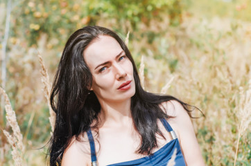 Attractive brunette among dry grass on the meadow. Summer mood. Travel and adventure, hikes.