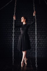 Ballerina in black dress and Pointe shoes in the background of a black brick wall. The room with the chains.