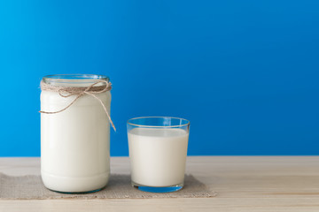 A bottle of rustic milk and glass of milk on a wooden table on a blue background, nutritious and healthy dairy products concept, farm natural products