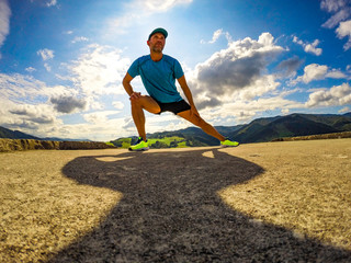 Male athlete runner stretching outdoors at sun and blue sky background. Side lunge stretch. - obrazy, fototapety, plakaty