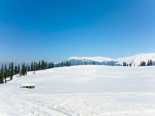 A house in snow valley with beautiful background of pines, hills and clear blue sky.
