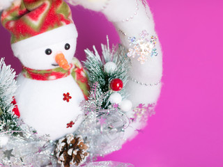 Close-up of snowman doll in white soft christmas wreath with many trinket decorations.