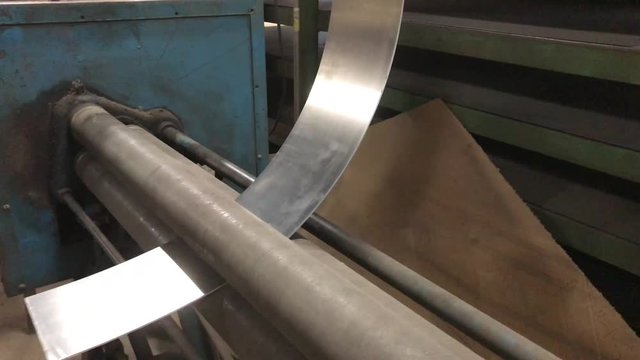 Fabricating a silver piece of sheet metal through plate roller machine to curve and bend product for fabrication use in welding machine shop.  