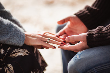 Cropped shot of young couple in love holding hands while sitting together outside. Focus on hands. Concept of Valentines Day. © Evgeniia Biriukova