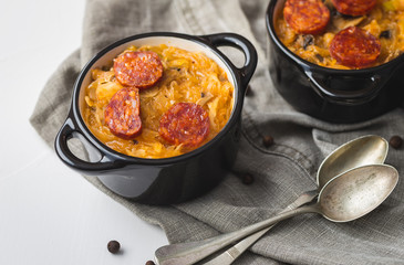 Slovak Christmas national cabbage soup in two small black pots with sausage on the tablecloth background.