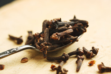 Dry cloves in metal spoon on a wooden table, closeup