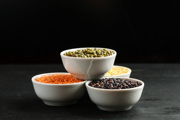 Set of different cereals and legumes in a white bowls on a black table