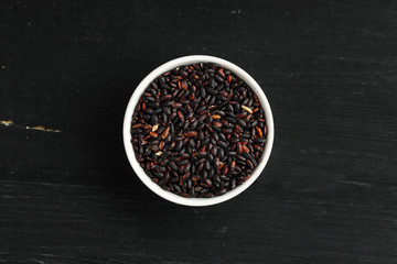 Black rice in a white bowl on a wooden table, top view