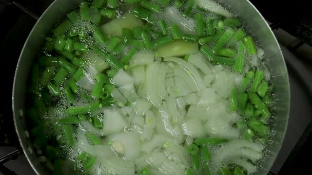 Close up of grean beans, potatoe and onions boiling in water.