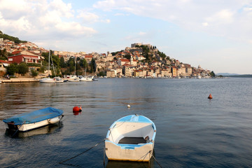 Fototapeta na wymiar Small rusty boat with a view of Sibenik in the background. Sibenik is popular summer travel destination.