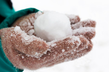 A girl in mittens holds a snowball. Winter fun in the outdoors_