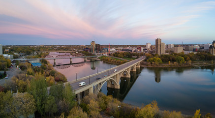 Fototapeta na wymiar Aerial panoramic view of a bridge going over Saskatchewan River during a vibrant sunrise in the Fall Season. Taken in Saskatoon, SK, Canada.