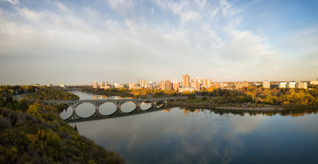 Aerial panoramic view of a bridge going over Saskatchewan River during a vibrant sunrise in the Fall Season. Taken in Saskatoon, SK, Canada.