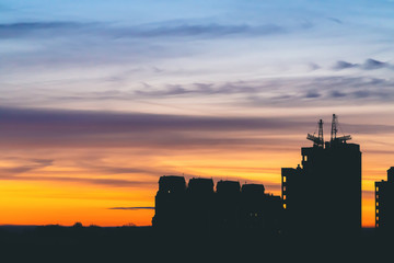Obraz premium Cityscape with wonderful varicolored vivid dawn. Amazing dramatic blue sky with purple and violet clouds above dark silhouettes of city buildings. Atmospheric background of orange sunrise. Copy space.