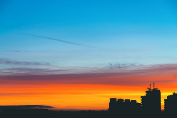 Fototapeta premium Cityscape with wonderful varicolored vivid dawn. Amazing dramatic multicolored cloudy sky above dark silhouettes of city buildings. Atmospheric background of sunrise. Orange sunlight. Copy space.