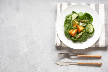 Green salad of spinach, yellow tomatoes and asparagus in a white ceramic plate. Grey background, top view