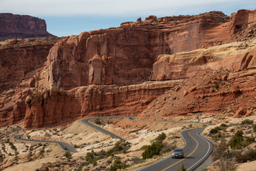 Fototapeta premium Scenic road in the red rock canyons during a vibrant sunny day. Taken in Arches National Park, located near Moab, Utah, United States.