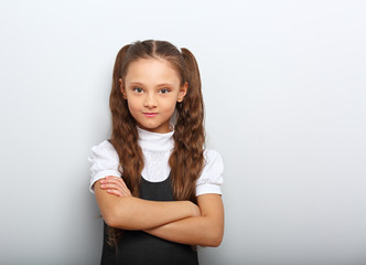 Fun pupil school girl with long hair style in uniform looking serious with folded arms on blue...