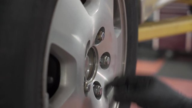Close up of white male auto mechanic replacing tire on car in auto shop