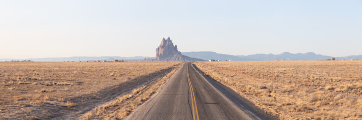 Panoramic View of a road in a dry desert with a Shiprock mountain peak in the background during a vibrant sunny sunrise.Taken at Rattlesnake, New Mexico, United States. © edb3_16