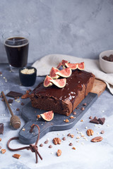 Square chocolate cake with chocolate cream, figs and blackberries on a gray background. Cold coffee in a glass and pine nuts.