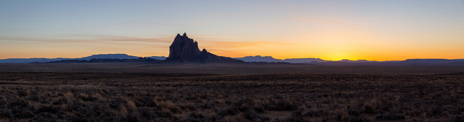 Striking panoramic landscape view of a dry desert with a mountain peak in the background during a vibrant sunset. Taken at Shiprock, New Mexico, United States.
