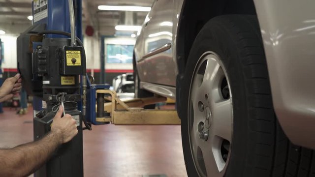 White male auto mechanic lowering car in auto shop