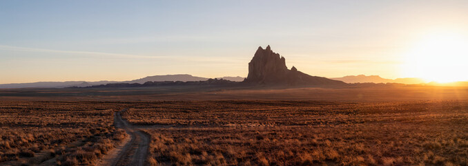 Striking panoramic landscape view of a dirt road in the dry desert with a mountain peak in the...