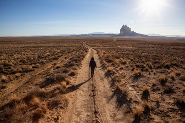 Woman walking on a dirt road in the dry desert with a mountain peak in the background. Taken at Shiprock, New Mexico, United States.